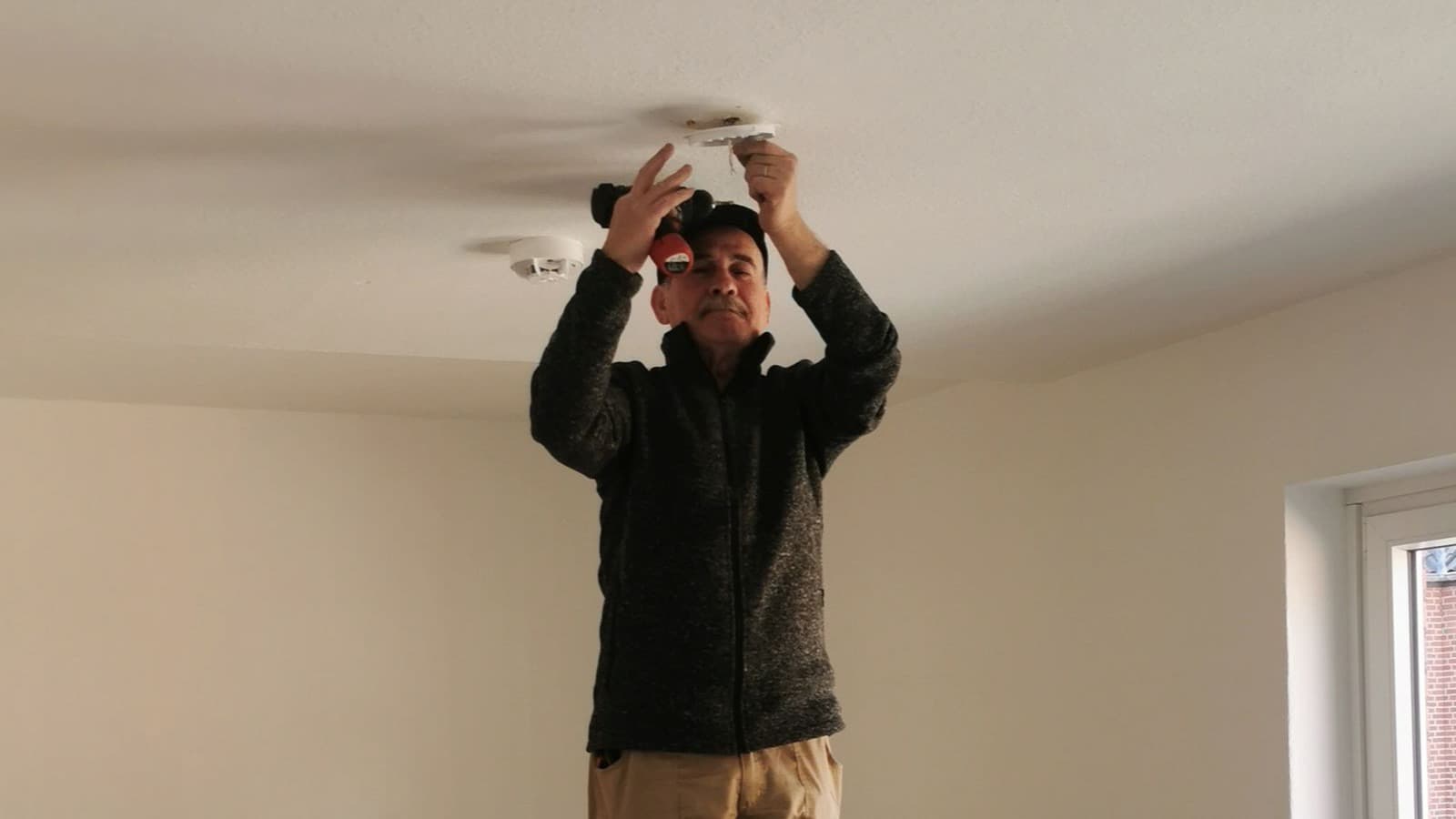 Handyman on a ladder installing a ceiling smoke detector in a Sacramento home during a home safety punch list visit